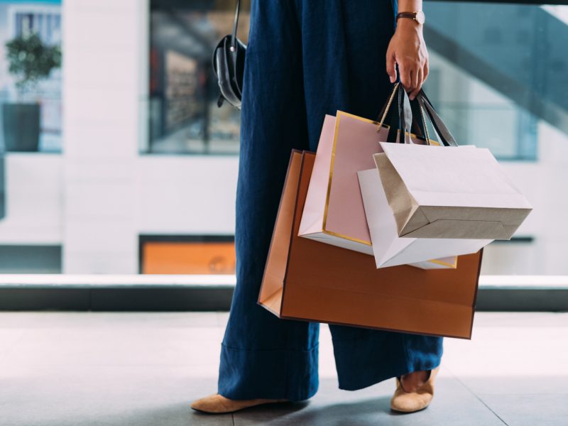 An unrecognizable Caucasian female standing at the shopping mall with paper bags.
